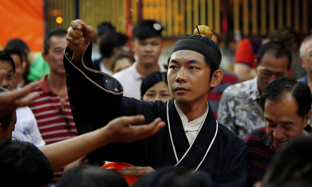 Thầy tu tung đồng xu để các tín đồ cầu may trong dịp lễ Ma Quỷ ở Malaysia.