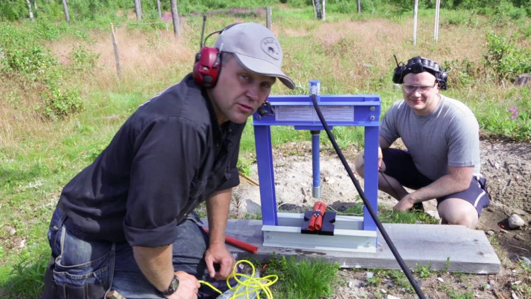 Hai người chuẩn bị làm thí nghiệm: dùng máy ép thủy lực ép lên khối thuốc nổ.