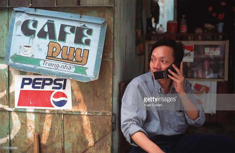 Một người đàn ông nói chuyện qua điện thoại di động tại một quán cà phê vỉa hè. 