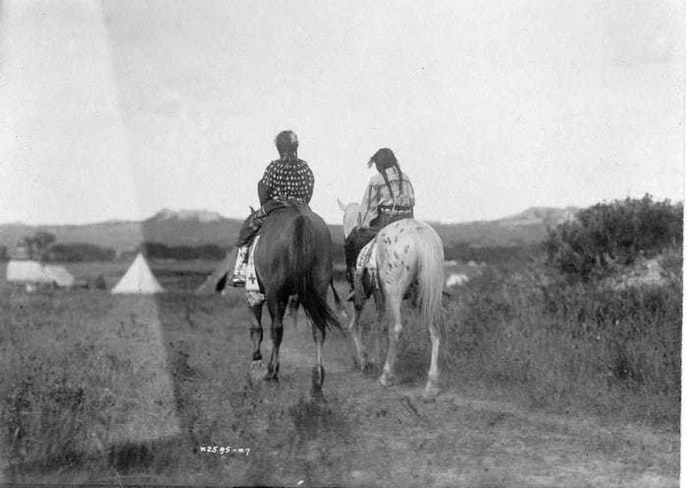 Hai cô con gái của một tù trưởng ngồi trên lưng ngựa hướng về phía những chiếc lều