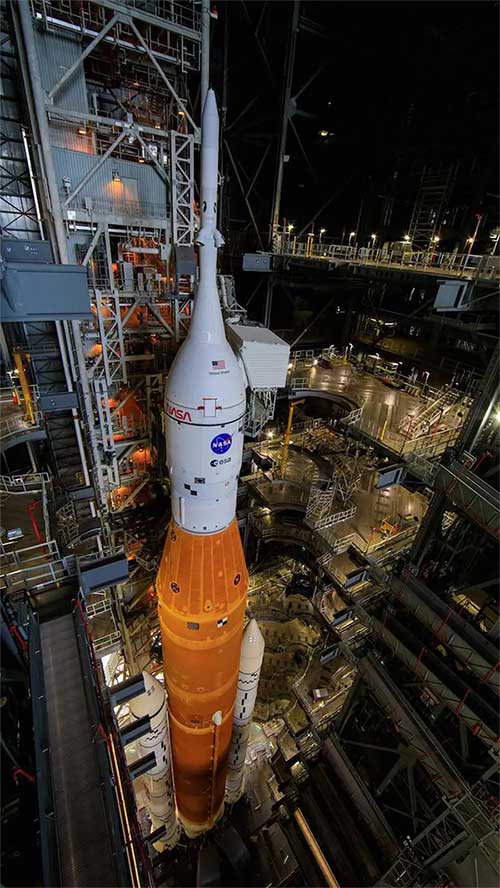 Hình ảnh tên lửa SLS với tàu vũ trụ Orion (màu trắng) gắn trên đỉnh, tại Tòa nhà Lắp ráp Phương tiện (VAB).