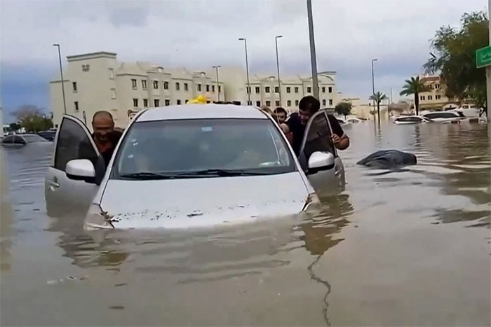Người dân cố gắng đẩy một chiếc ô tô bị mắc kẹt do lũ lụt bất thường ở Dubai hôm 16-4
